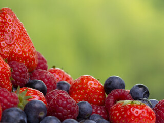 Pile of strawberries, blueberries, raspberries on green background