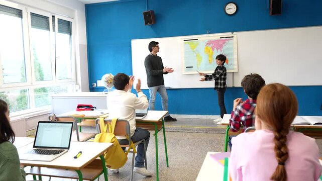 Young students presenting their geography project using a world map in front of their classmates and teacher