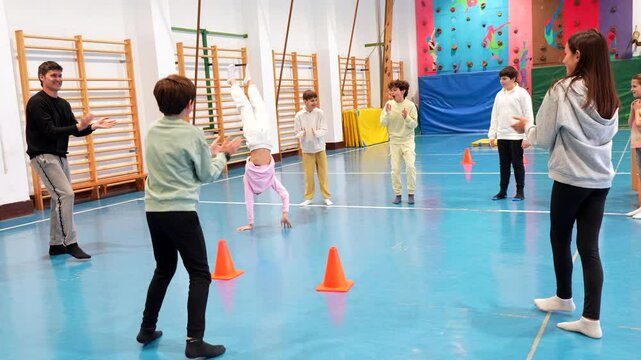 Young students developing physical skills while learning challenging handstands with professional instructor during engaging gym class, focusing on coordination and balance