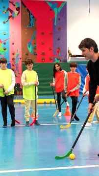 Dedicated coach guiding students through floorball skills and teamwork during physical education class in school gymnasium
