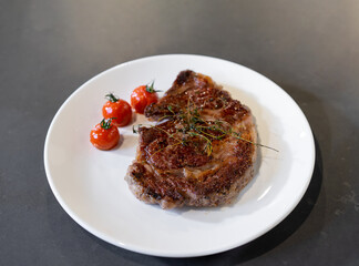 Cooked and grilled steak on white dish with a little tomato with it, ready for the next decoration step.