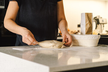 Hands are skillfully rolling and shaping dough on a clean kitchen countertop sprinkled with flour, healthy sourdough bread. The bright space suggests a cozy baking atmosphere.