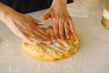 Hands are skillfully rolling and shaping dough on a clean kitchen countertop sprinkled with flour, healthy sourdough bread. The bright space suggests a cozy baking atmosphere.