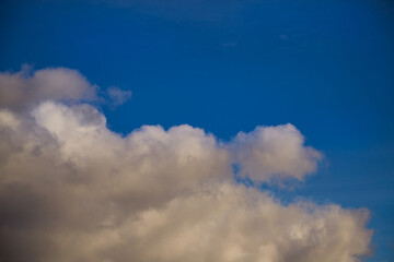 White cumulus clouds with shades of golden sunlight fill the sky, creating a sense of depth and...