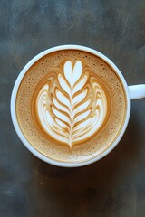 Cup of latte featuring detailed leaf art design at the center, resting on a gray surface, ideal for a relaxing morning coffee experience