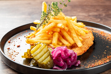 A delicious plate featuring crispy golden French fries atop a crispy chicken fillet, garnished with fresh thyme. Served alongside pickles and sweet pickled onions for a flavorful contrast.