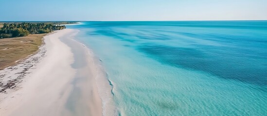 Aerial view of a pristine tropical beach with crystal-clear turquoise waters gently lapping the white sand shoreline, palm trees lining the coast under a vast blue sky dotted with fluffy clouds