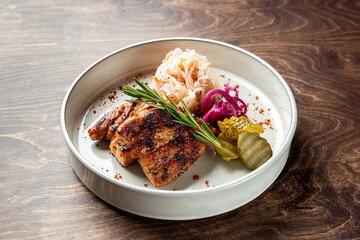 Grilled pork fillet served on a white plate with pickled vegetables, sauerkraut, and fresh herbs. A colorful and appetizing display perfect for restaurant menus or food blogs.
