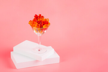 Fruit flavored worm shape, jelly candies in a glass on pink background. 