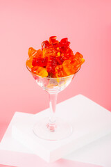 Fruit flavored worm shape, jelly candies in a glass on pink background.