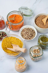 Assortment of cereals and legumes in jars, containers and bowls on a light background. Healthy eating, products, vegetarianism.