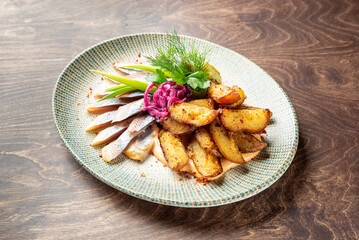 A beautifully arranged plate featuring roasted potatoes, pickled purple onions, and succulent slices of fish. The dish is garnished with fresh herbs, set against a rustic wooden background.