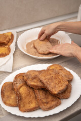 Close-up of hands coating freshly fried torrijas in cinnamon sugar on a kitchen counter