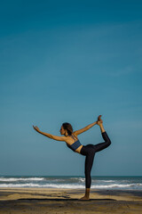 Young caucasian woman practicing yoga on beach in balancing pose at sunset