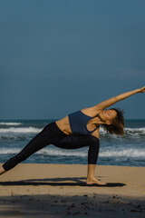 Young asian female practicing yoga on beach in athletic wear
