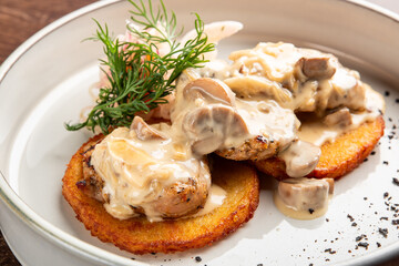 A delicious plate featuring golden, crispy potato pancakes topped with tender chicken and rich mushroom cream sauce, garnished with fresh herbs. Perfect for food enthusiasts.