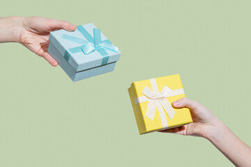 Two blue and yellow gift boxes in hands on light green  background.
