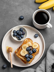Peanut butter toast with banana and blueberry on a plate on a dark  background with a cup of espresso coffee