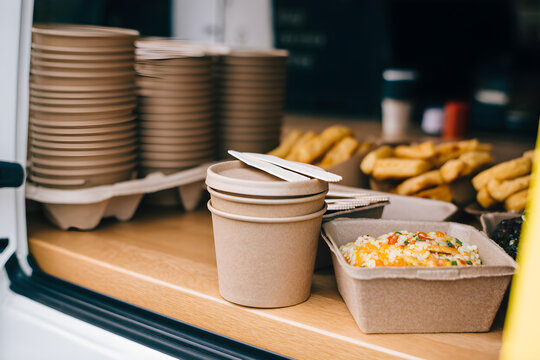 Bright yellow food truck serving drinks with two smiling servers in casual attire at a bustling outdoor location during the day. Two young servers, a man and a woman, smile while holding paper cups. 