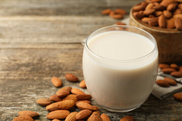 Fresh almond milk in glass and nuts on wooden table, closeup