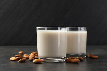 Fresh almond milk in glasses and nuts on dark grey table