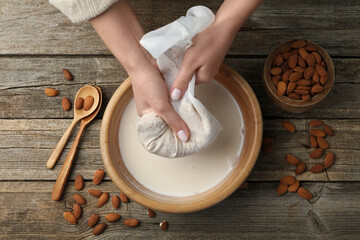 Woman making almond milk at wooden table, top view