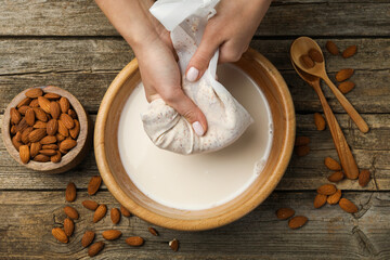 Woman making almond milk at wooden table, top view