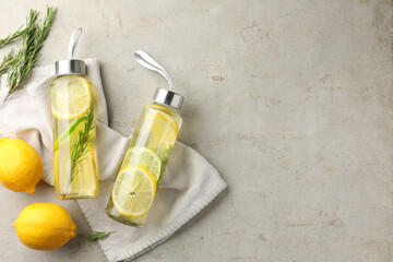 Lemon water with lime in bottles, rosemary and fresh fruits on grey table, flat lay. Space for text