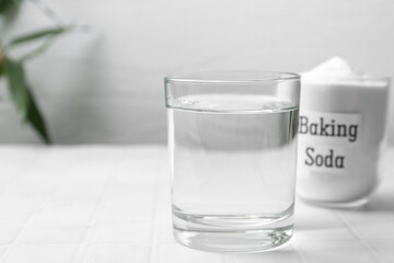 Glass of water and baking soda on white tiled table. Space for text