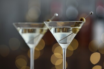 Martini cocktail with olives in glasses on blurred background, closeup. Bokeh effect