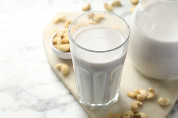 Fresh cashew milk in glass and nuts on white marble table, closeup. Space for text