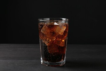 Refreshing cola with ice cubes in glass on black wooden table, closeup