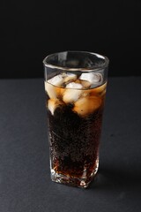 Refreshing cola with ice cubes in glass on black table, closeup