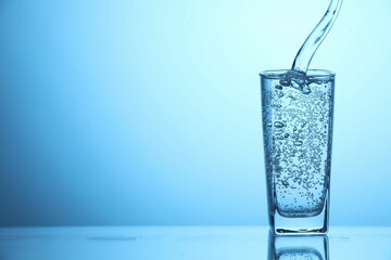Pouring soda water into glass on light blue background, closeup. Space for text