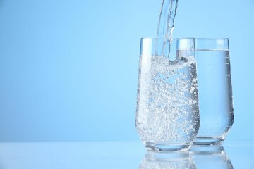 Pouring refreshing soda water into glasses on light blue background, closeup. Space for text