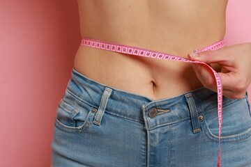 Woman measuring waist circumference on pink background, closeup