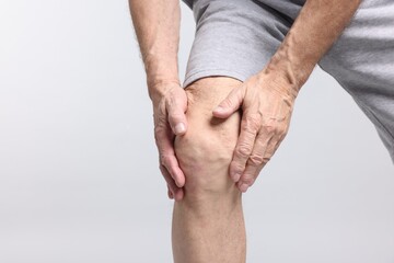 Senior man suffering from knee pain on light grey background, closeup