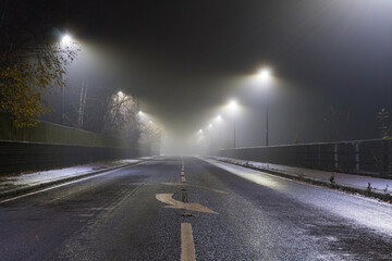 A long straight road, with an arrow painted on the road. On a mysterious foggy night