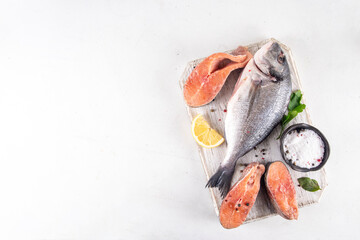 Raw fish and seafood cooking background, various fresh whole and sliced fish with spices, lemon, olive oil for preparation dinner, white table background copy space
