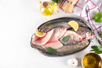 Raw fish and seafood cooking background, various fresh whole and sliced fish with spices, lemon, olive oil for preparation dinner, white table background copy space