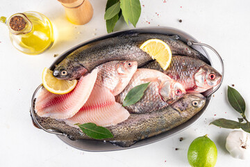 Raw fish and seafood cooking background, various fresh whole and sliced fish with spices, lemon, olive oil for preparation dinner, white table background copy space