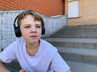 A young boy relaxes on the steps of a building, wearing headphones and lost in thought. He appears contemplative as he enjoys his listening experience in a calm environment