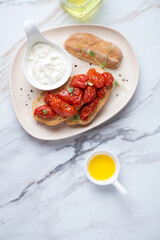 Stracciatella cheese and roasted tomato bruschettas, vertical shot on a white stone background with space, flat lay