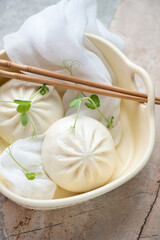 Serving tray with steamed baozi buns and fresh pea sprouts, vertical shot on a roseate granite background, middle closeup