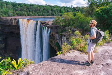 A stunning view of Kaieteur Falls in Guyana, with lush green forests and a man admiring the view