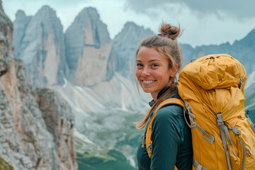 Naklejka premium A smiling female traveler with a yellow hiking backpack enjoys the beautiful scenery of the majestic mountains. Travel, adventure. Concept of an active lifestyle