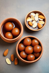 Gulab jamun in small clay pots, arranged on a table with one pot of sweet water and some scattered almond nuts.