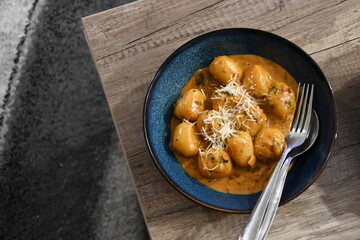color photo of a dish of potato gnocchi sprinkled with parmesan, in a pepper sauce, with herbs, traditional homemade tasty food, close up view