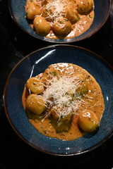 color photo of a dish of potato gnocchi sprinkled with parmesan, in a pepper sauce, with herbs, traditional homemade tasty food, close up view