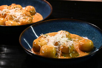 color photo of a dish of potato gnocchi sprinkled with parmesan, in a pepper sauce, with herbs, traditional homemade tasty food, close up view